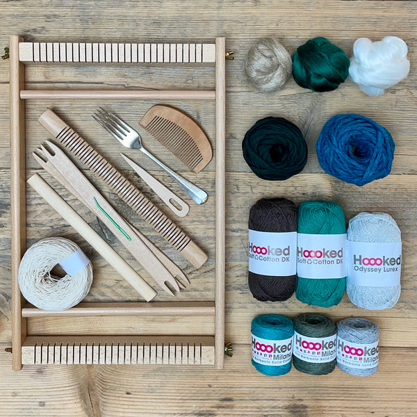 A beginners frame/ tapestry loom weaving starter kit displayed with weaving supplies including assorted yarns in an 'Marine' colour way and weaving tools.