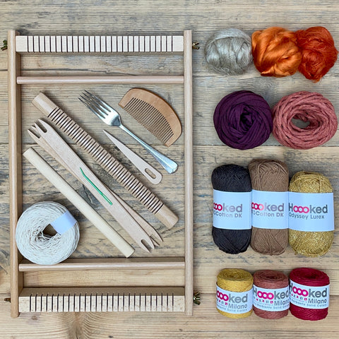 A beginners frame/ tapestry loom weaving starter kit displayed with weaving supplies including assorted yarns in an 'Autumn' colour way and weaving tools.