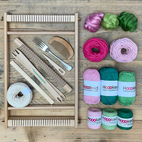 A beginners frame/ tapestry loom weaving starter kit displayed with weaving supplies including assorted yarns in an 'Blossom' colour way and weaving tools.