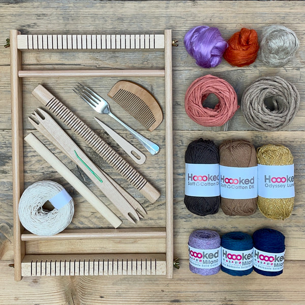 A beginners frame/ tapestry loom weaving starter kit displayed with weaving supplies including assorted yarns in an 'Canyon' colour way and weaving tools.