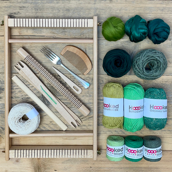 A beginners frame/ tapestry loom weaving starter kit displayed with weaving supplies including assorted yarns in an 'Forest' colour way and weaving tools.
