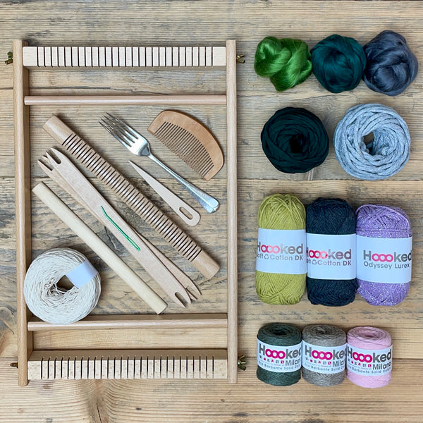 A beginners frame/ tapestry loom weaving starter kit displayed with weaving supplies including assorted yarns in an 'Highlands' colour way and weaving tools.