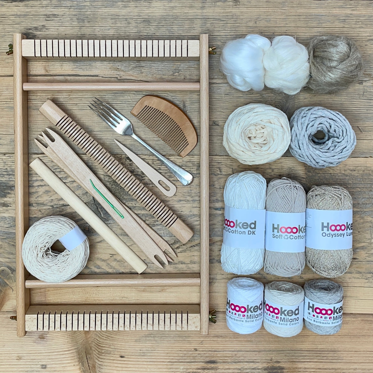 A beginners frame/ tapestry loom weaving starter kit displayed with weaving supplies including assorted yarns in a 'Natural' colour way and weaving tools.