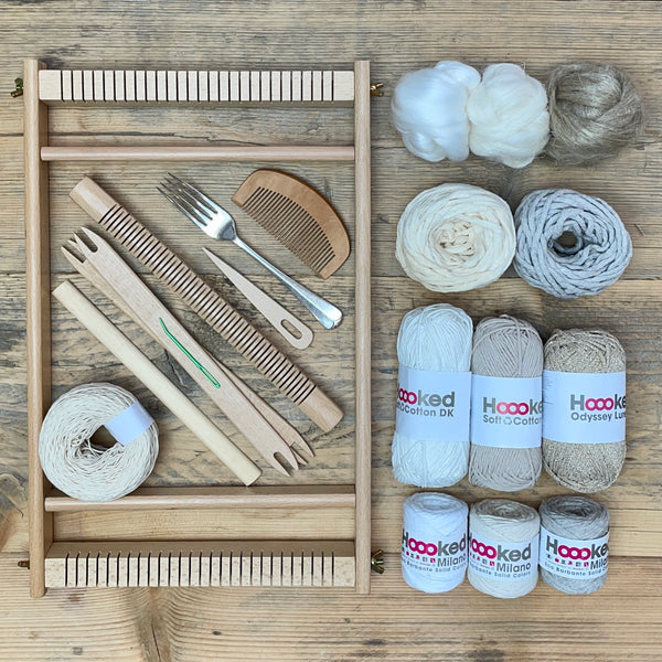 A beginners frame/ tapestry loom weaving starter kit displayed with weaving supplies including assorted yarns in an 'Natural' colour way and weaving tools.