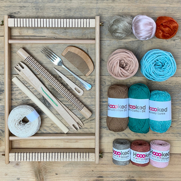 A beginners frame/ tapestry loom weaving starter kit displayed with weaving supplies including assorted yarns in an 'Santa Fe' colour way and weaving tools.