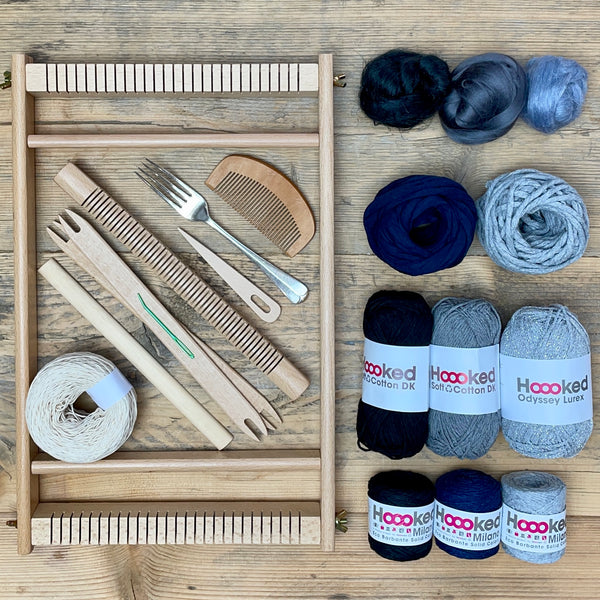 A beginners frame/ tapestry loom weaving starter kit displayed with weaving supplies including assorted yarns in an 'Storm' colour way and weaving tools.